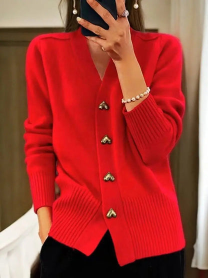Bright red version of the cardigan worn by a model, showing gold heart buttons down the front and ribbed trim, with black trousers. 4
