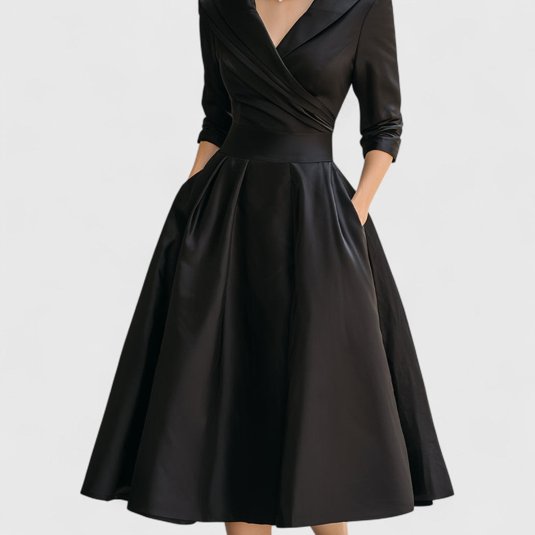 Black midi dress shown on a plain pale background, cropped to highlight the wrap bodice, waistband and full pleated skirt. 11