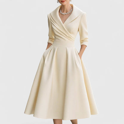Cream version of the A-line midi dress with pleated wrap bodice, shawl collar and three-quarter sleeves on a model. 4