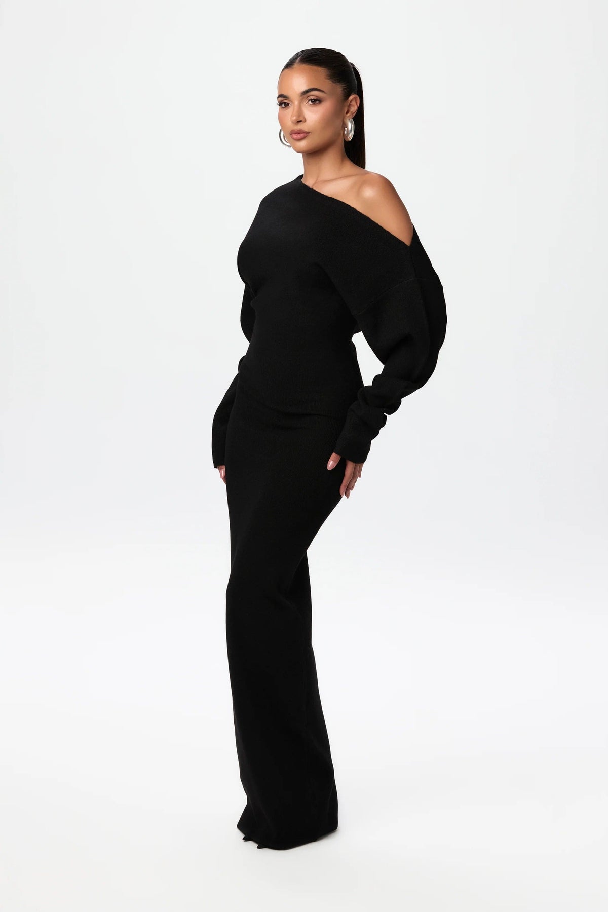 Three-quarter side view of the black off-the-shoulder knit maxi dress, showing the full sleeve and slim fit. 2