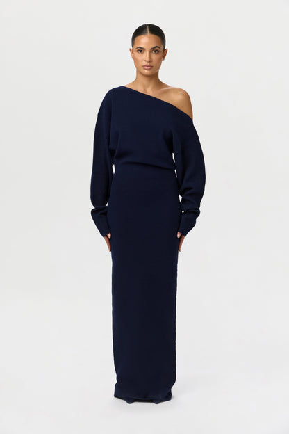 Front view of the navy knit maxi dress worn off one shoulder, with a defined waist seam and fitted long skirt. 24