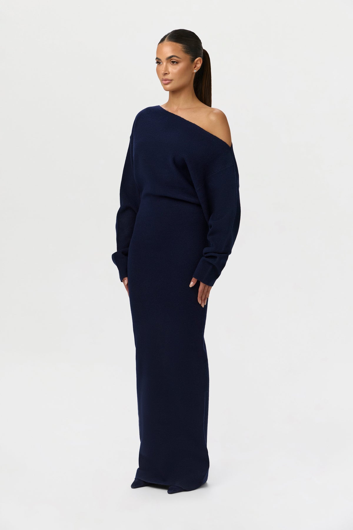 Side angle of the navy knit maxi dress, showing the off-the-shoulder neckline, loose long sleeves and slim floor-length skirt. 25
