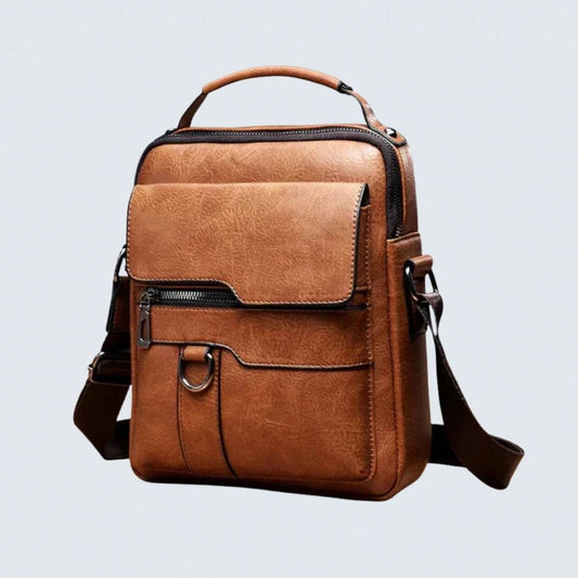 Tan faux-leather shoulder bag seen at a three-quarter angle on a pale grey background, with top handle and front flap pocket. 1
