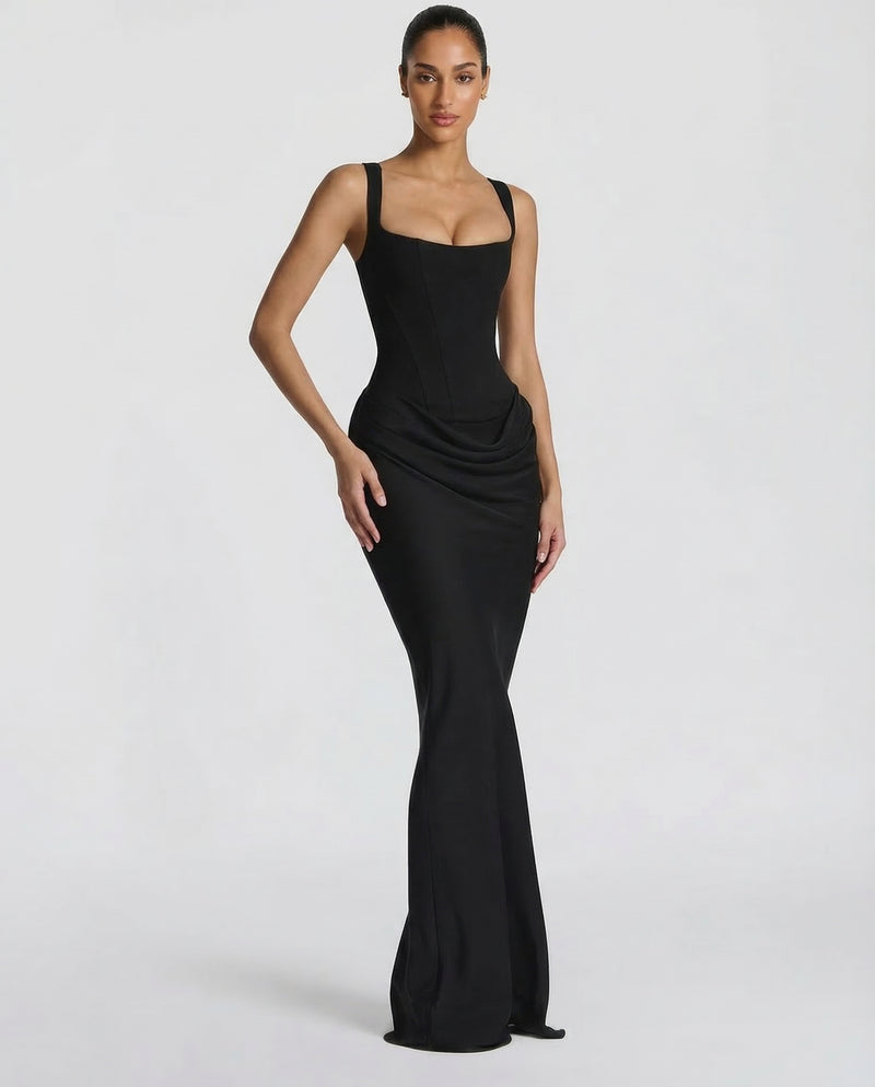 Black corset maxi dress worn at a three-quarter angle, one hand on hip, showing the draped hip and fitted fishtail skirt. 4