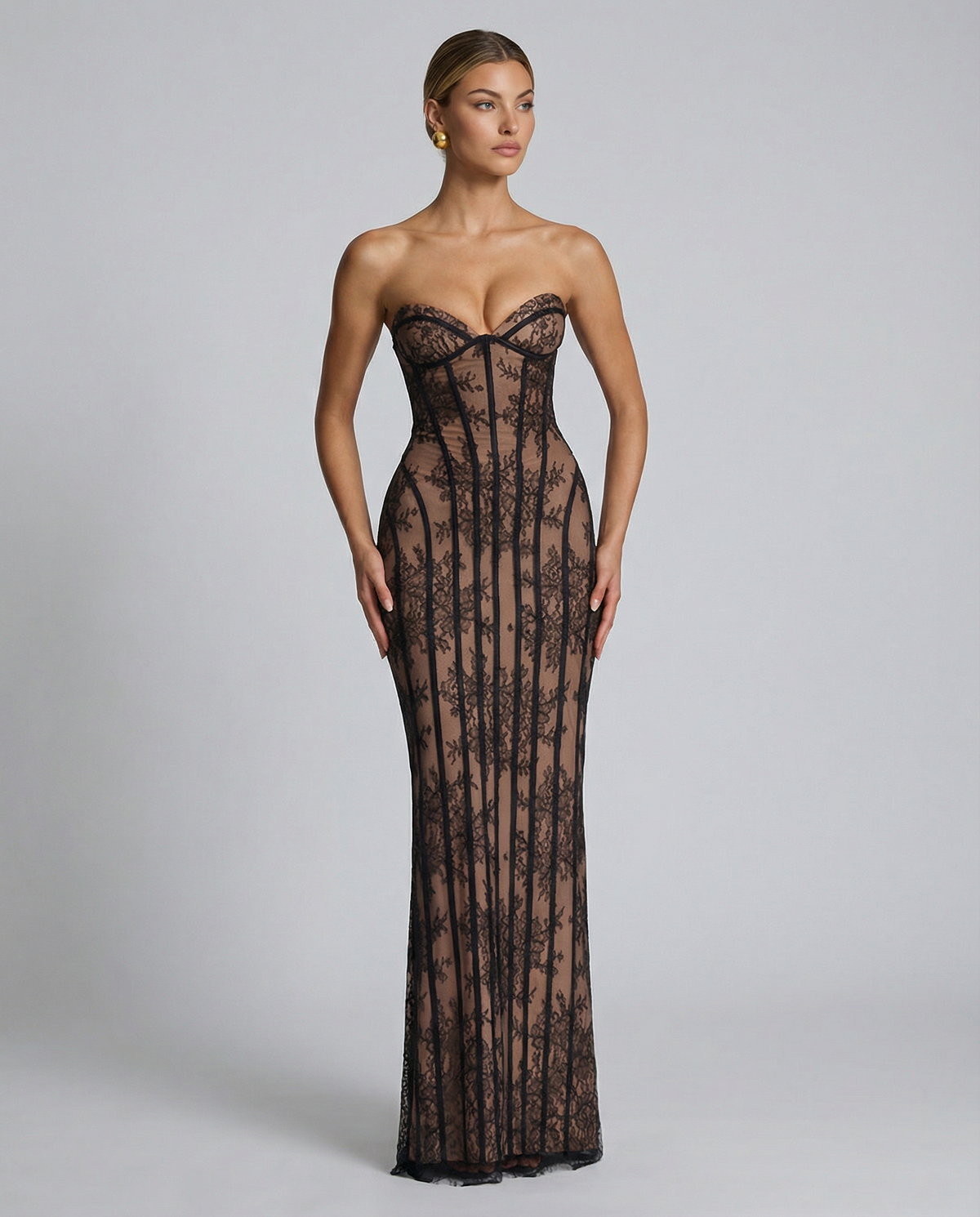 Model standing straight in the black floral lace dress against a grey backdrop, wearing gold earrings with her hair slicked back. 8