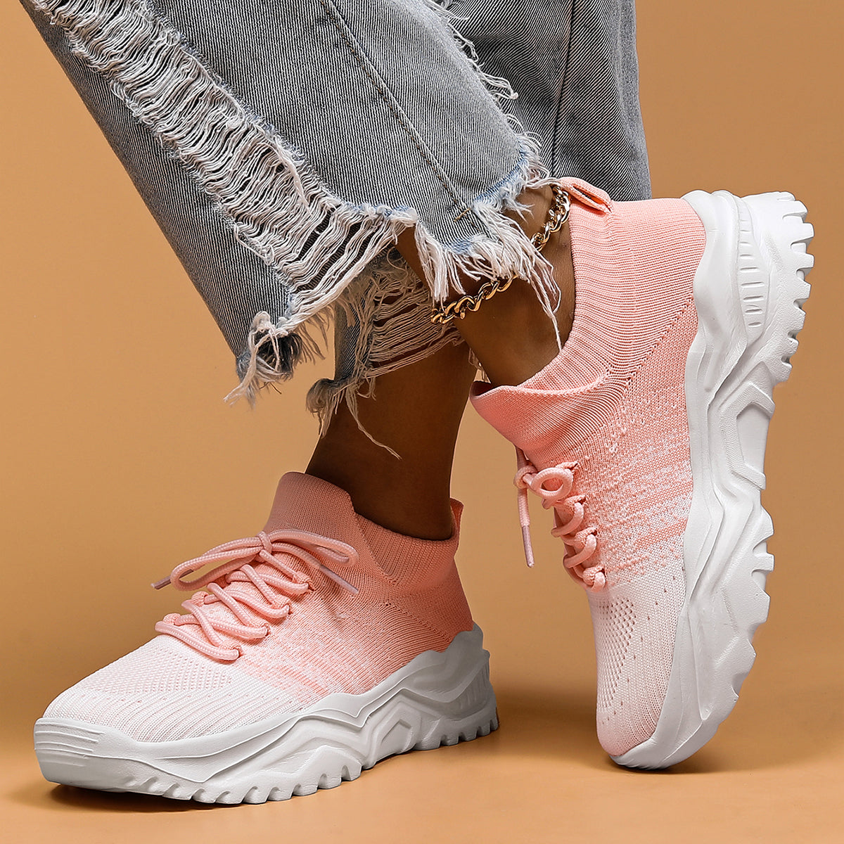 Pink and white knit lace-up sneakers with chunky white soles, worn with frayed grey jeans and a gold chain anklet. 6