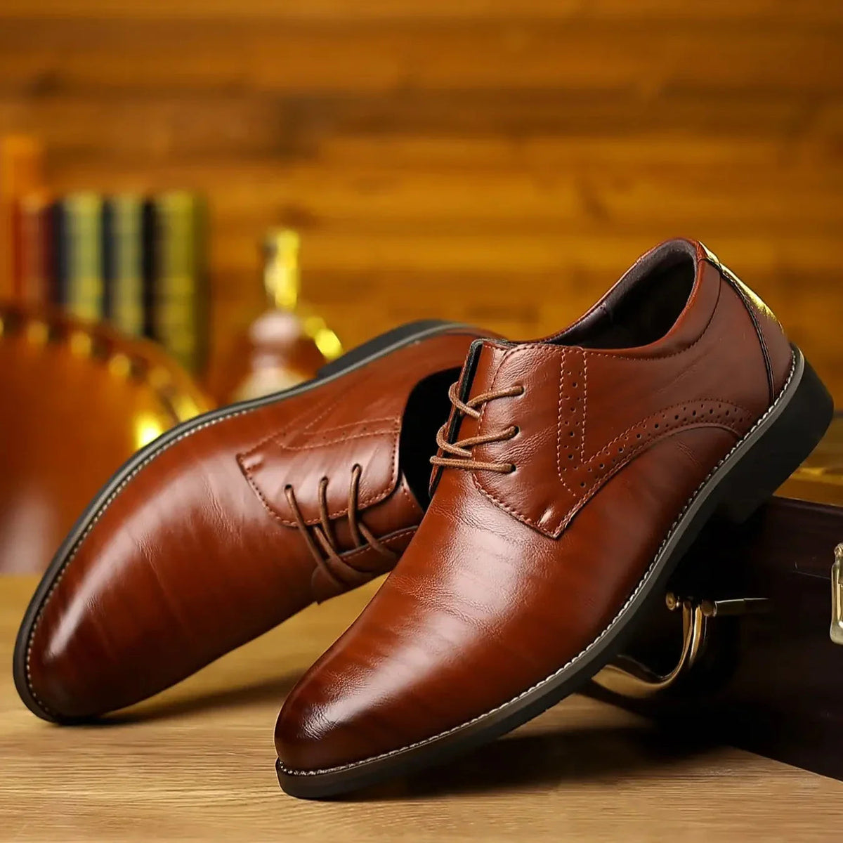 Pair of glossy tan-brown leather lace-up shoes with brogue detailing, resting on a wooden table against a warm, blurred background. 1