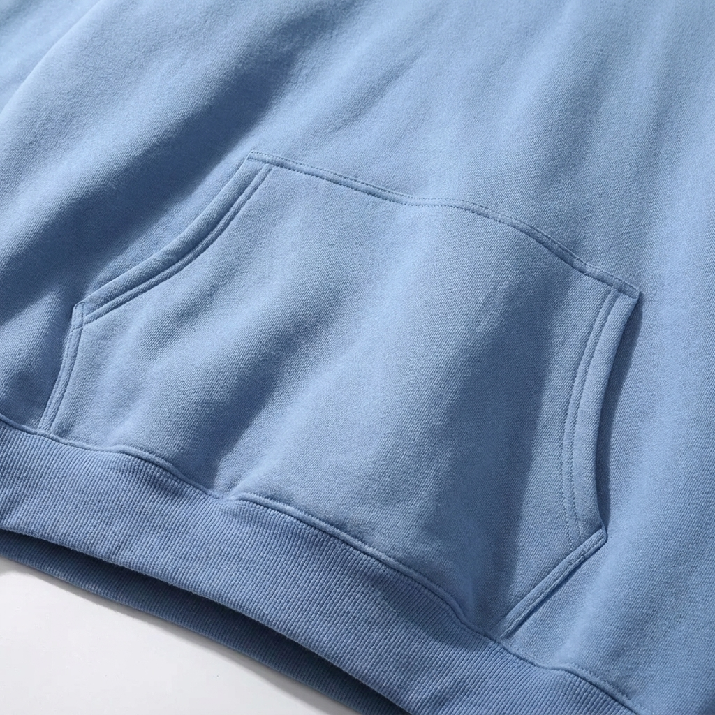 Close-up of the front kangaroo pocket and ribbed hem on a light blue fleece-backed hoodie, showing the stitching detail. 4