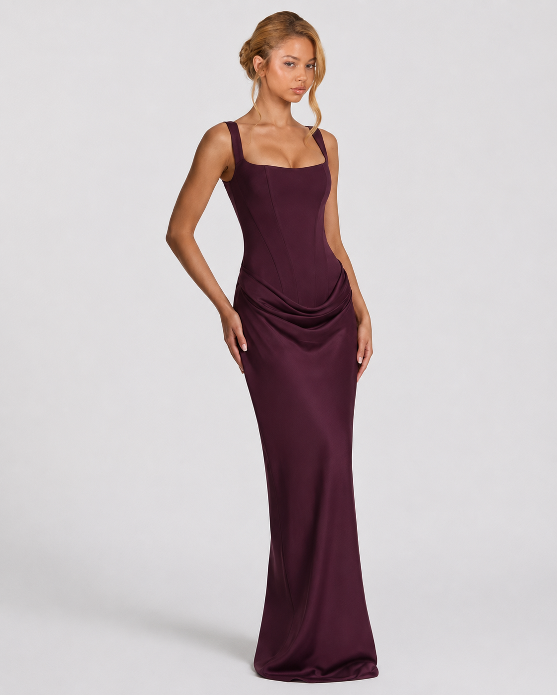 Plum corset maxi dress worn at a three-quarter angle, hand on hip, showing the draped hip and fluid satin skirt. 15