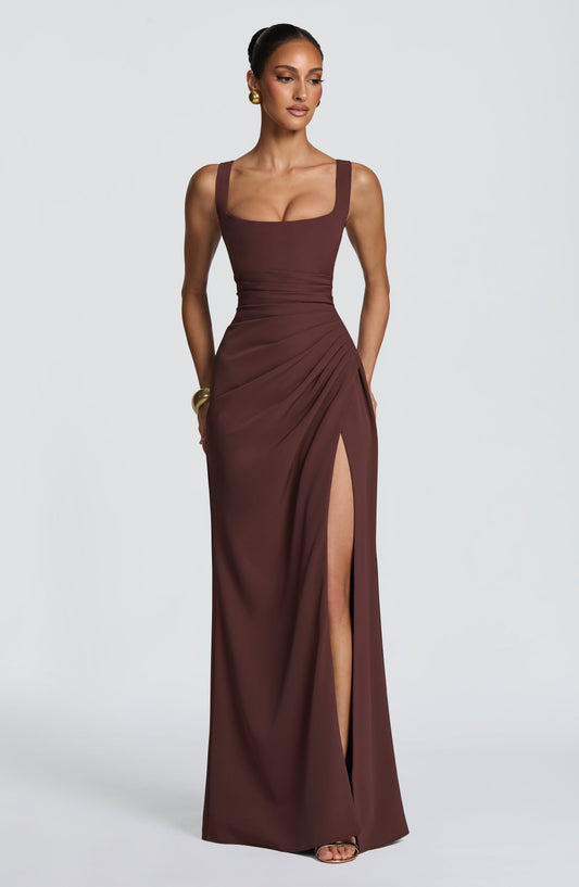 Model wearing the brown square-neck maxi dress, facing forward with ruched waist, high side slit and gold jewellery. 1