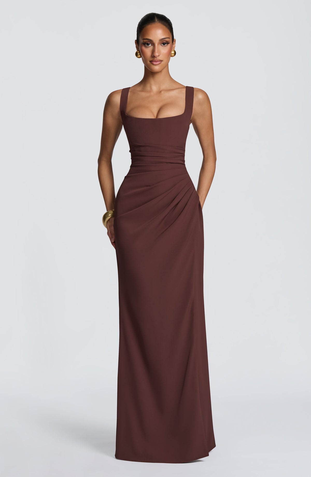Front view of the brown maxi dress on a model with hands behind her, showing ruched waist and fitted bodice. 4