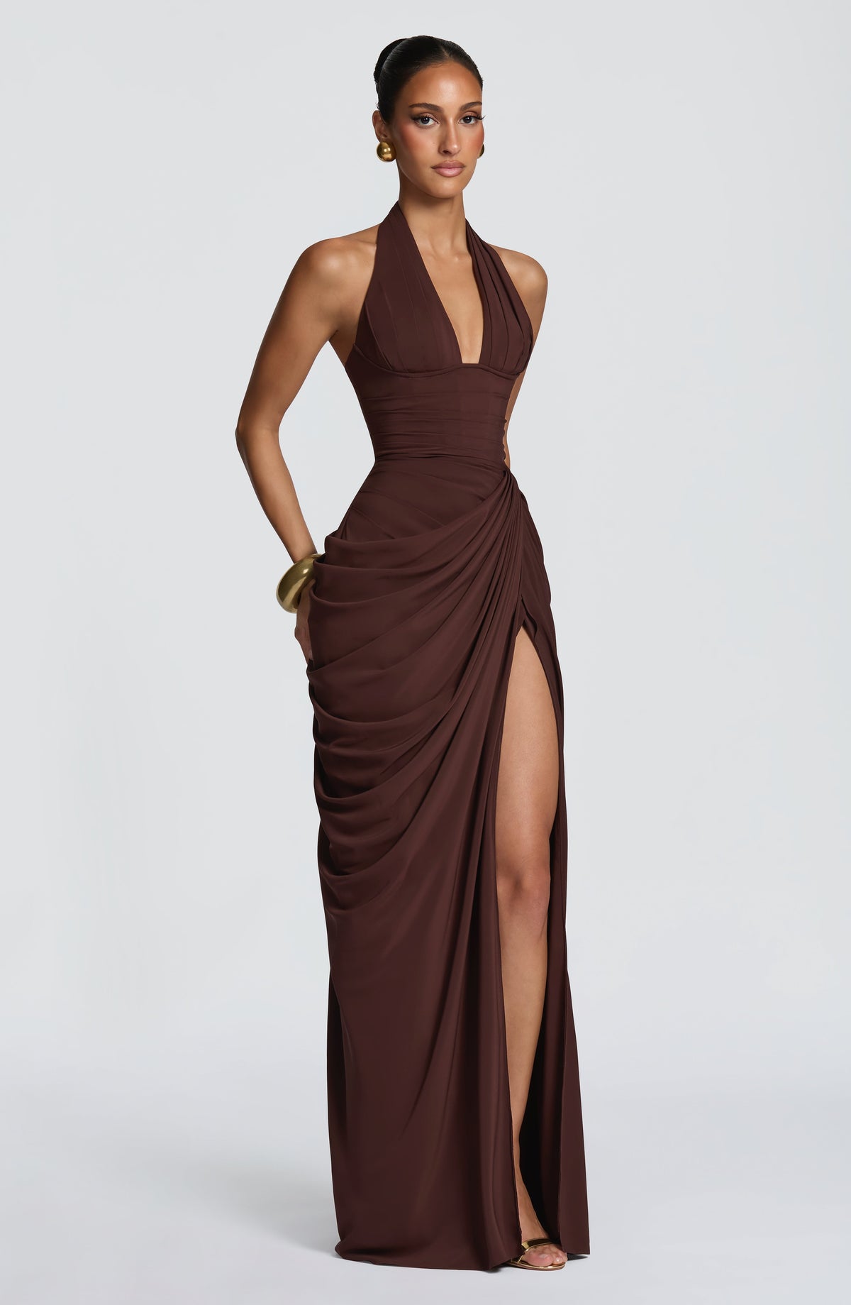 Three-quarter view of the brown dress on a model, hand resting at the hip, with the thigh split opening. 27