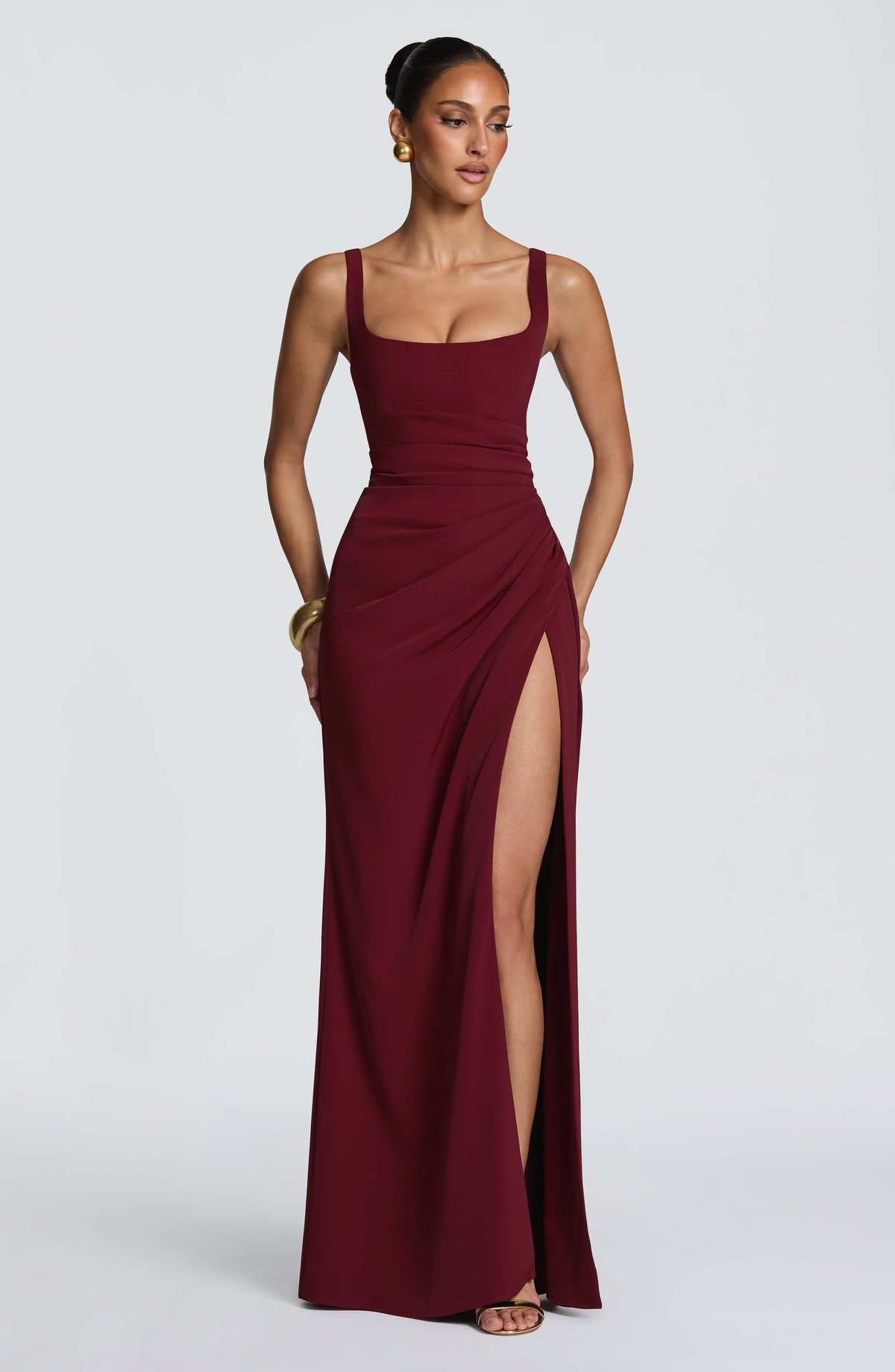 Model wearing the burgundy version of the maxi dress, with gold bangle and earrings, high slit visible. 17
