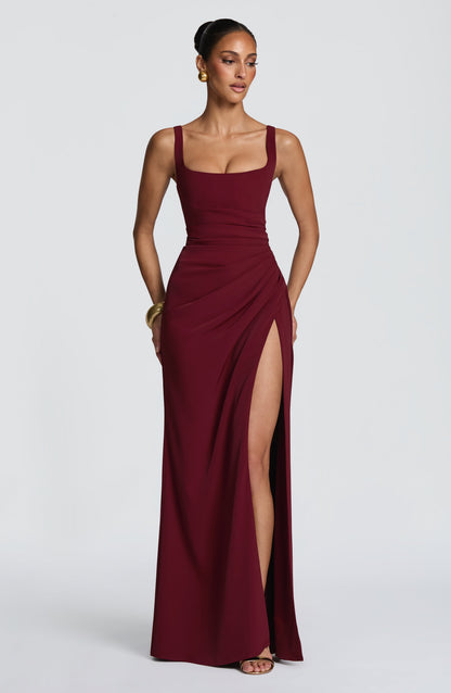 Model wearing the burgundy version of the maxi dress, with gold bangle and earrings, high slit visible. 17