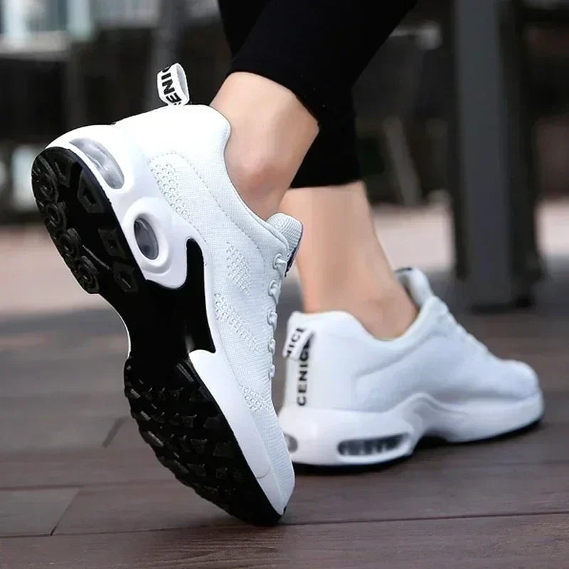 Rear three-quarter view of white knit trainers in mid-stride, showing the black tread, air-cushion window and heel pull tab. 3