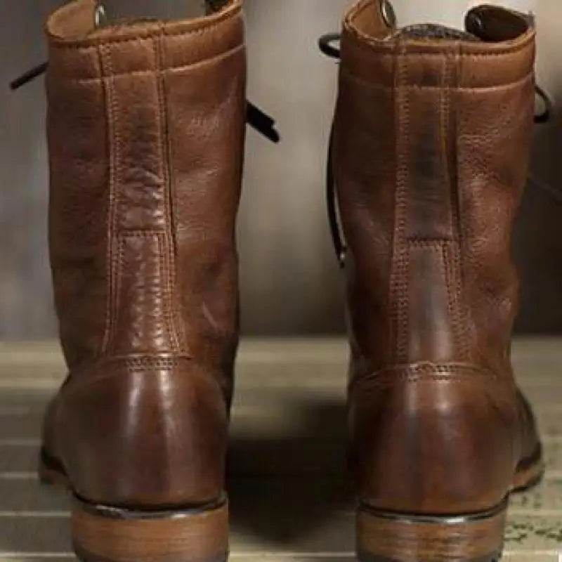 Back view of two brown leather boots showing the vertical heel stitching, stacked heels and loosely trailing laces. 2