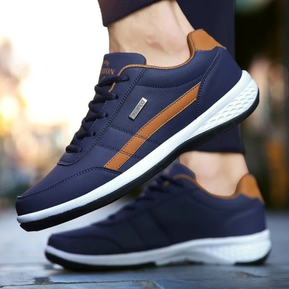 Navy sneakers with tan side stripes worn by a walker in dark trousers, one foot raised to show the side. 7