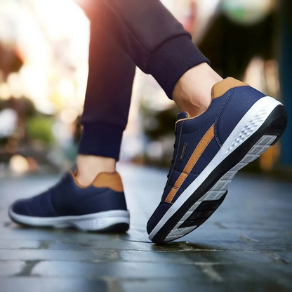 Rear three-quarter view of navy sneakers with tan heel tabs worn mid-stride, showing the patterned tread underneath. 8