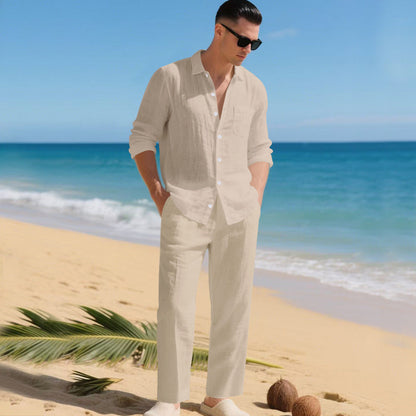 Man in sunglasses on a sandy beach wearing the cream long-sleeved shirt and matching straight trousers, hands in pockets. 4