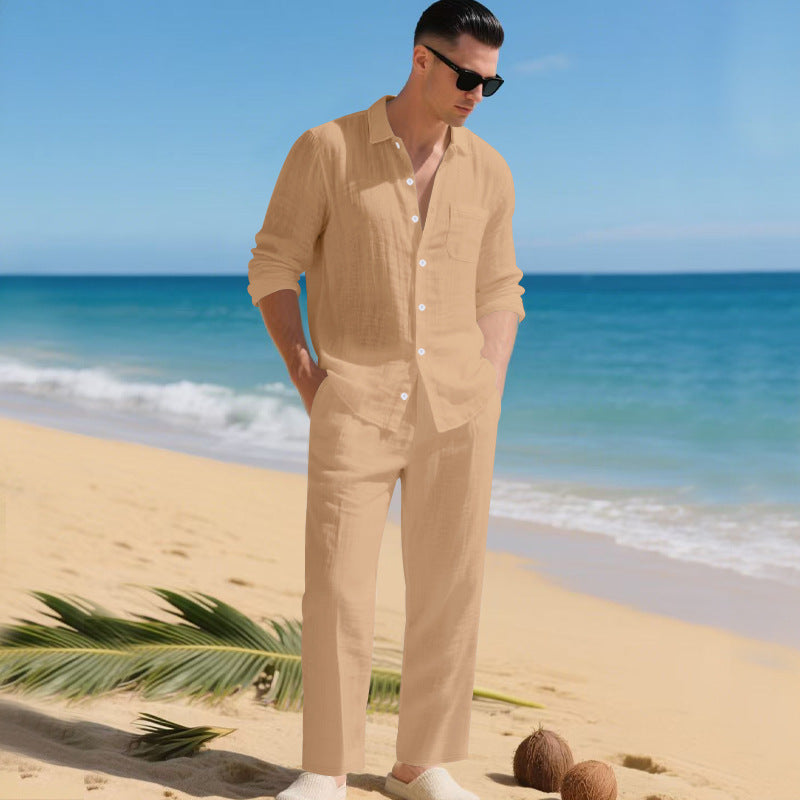 Man in sunglasses on a sandy beach wearing the sand-coloured long-sleeved shirt and matching straight trousers, hands in pockets. 5