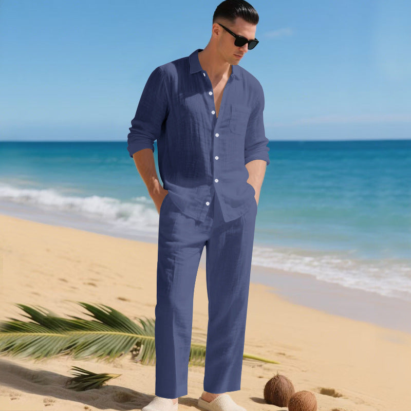 Man in sunglasses on a sandy beach wearing the navy blue long-sleeved shirt and matching straight trousers, hands in pockets. 6