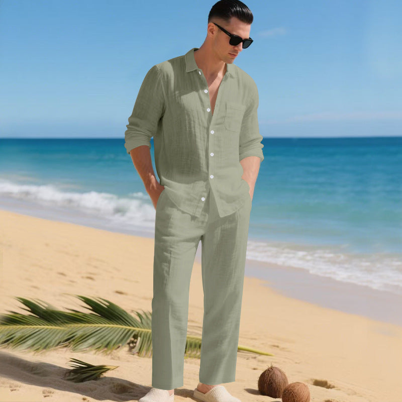 Man in sunglasses on a sandy beach wearing the sage green long-sleeved shirt and matching straight trousers, hands in pockets. 7