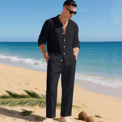 Man in sunglasses on a sandy beach wearing the black long-sleeved shirt and straight trousers, hands in pockets. 1