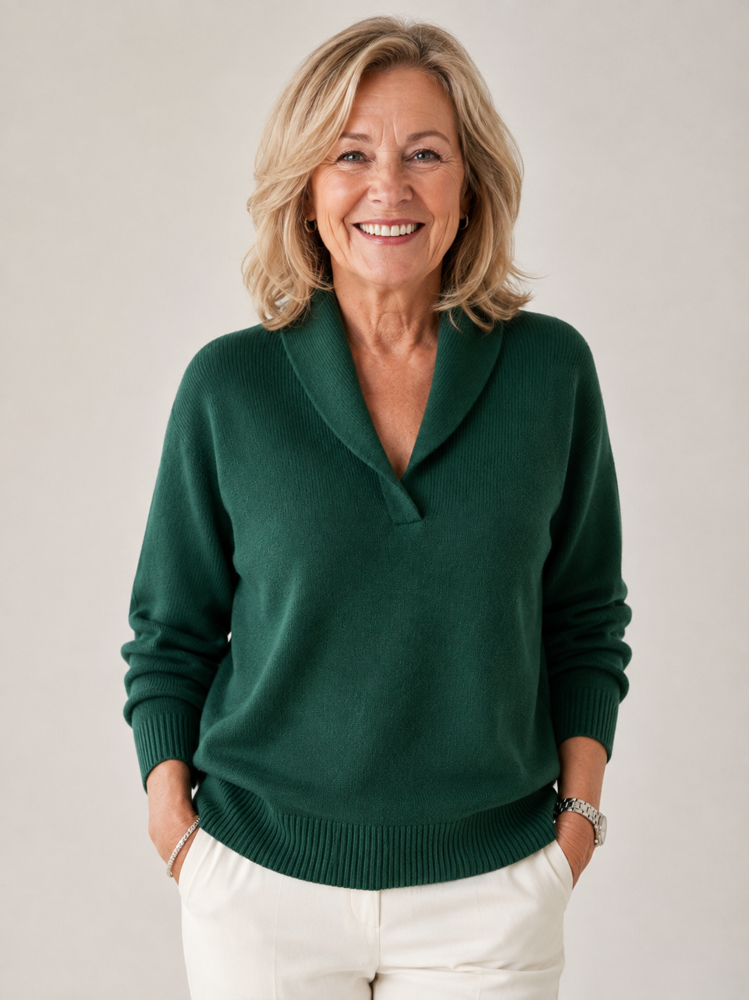 Full-length front view of a smiling woman in the dark green jumper, hands in the pockets of white trousers. 9