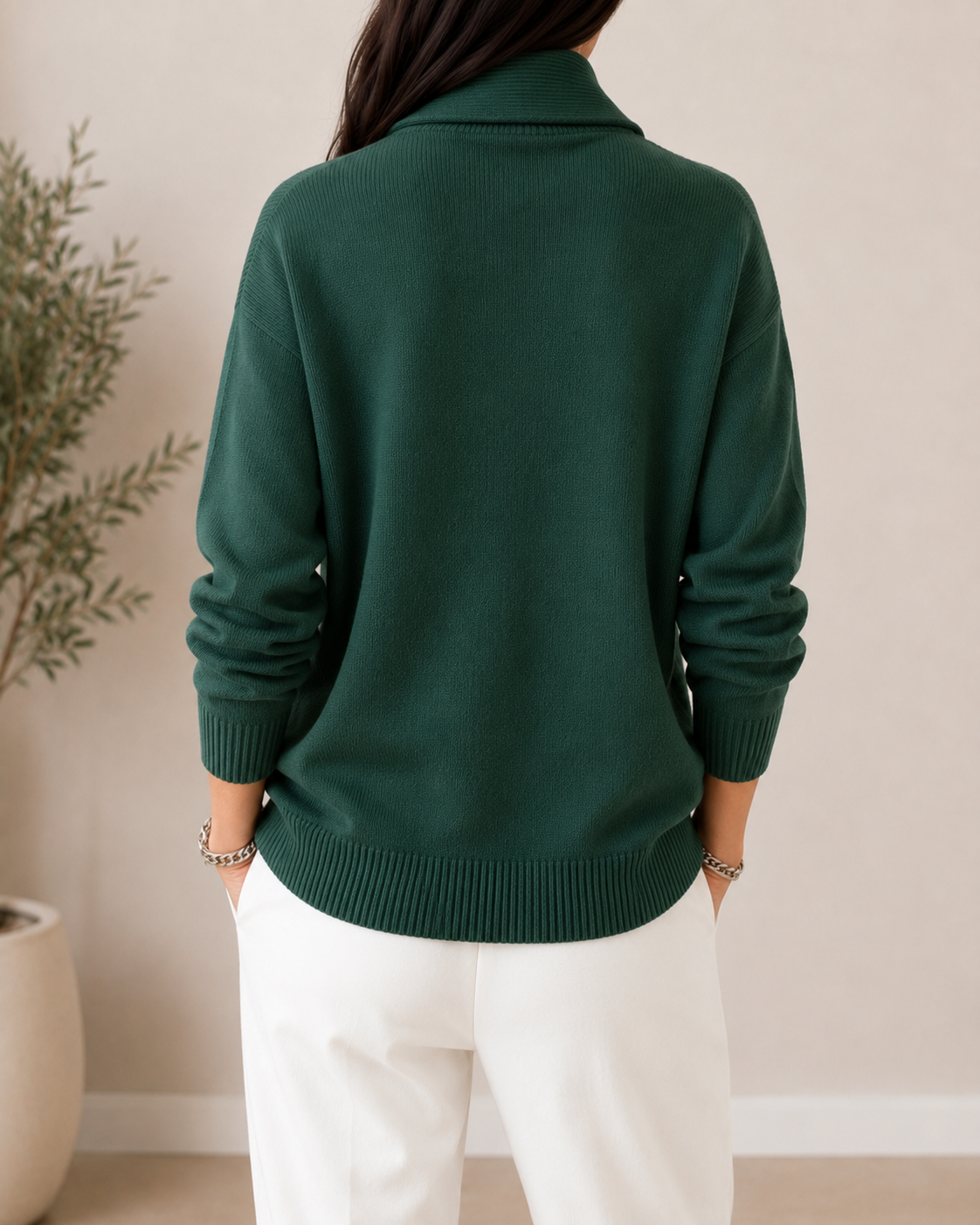 Back view of the dark green jumper worn with white trousers, showing the plain back and ribbed hem. 11