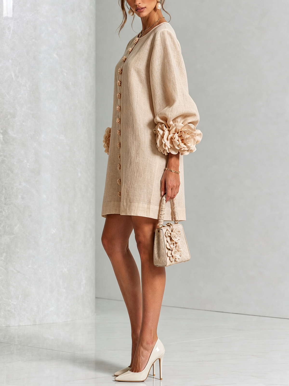 Beige dress in side view on a model with cream heels and a floral bag, showing the voluminous sleeve and rosette cuff. 28