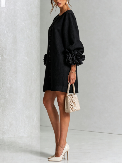 Black dress seen from the side on a model with cream heels and a small floral handbag, showing the puffed sleeve and rosette cuff. 22