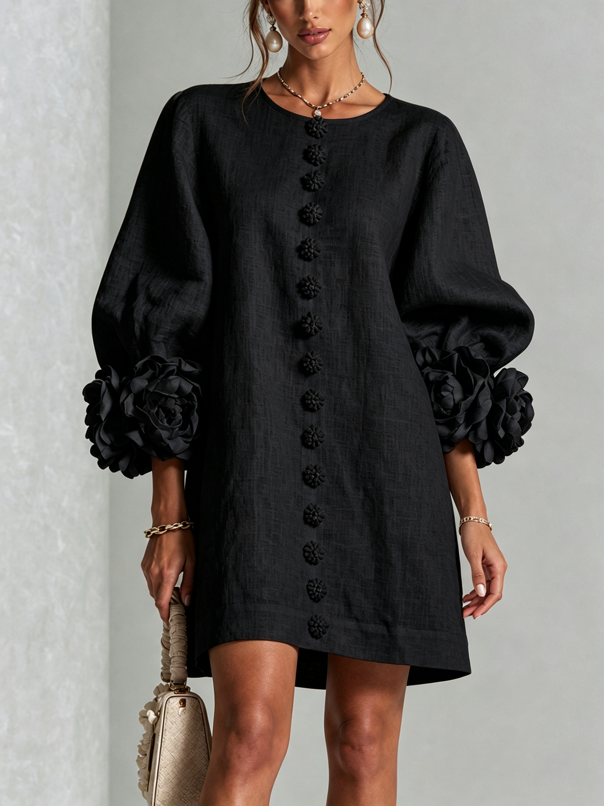 Black short dress worn by a model, front view, with a row of fabric flower buttons and large rosettes on the puffed sleeve cuffs. 21