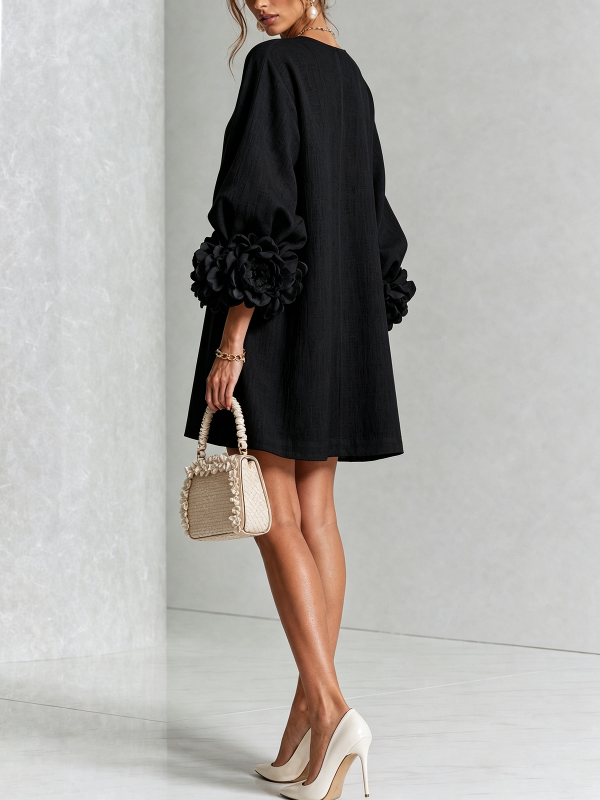Black dress seen from behind on a model glancing over her shoulder, showing the plain back and large rosette cuffs. 23