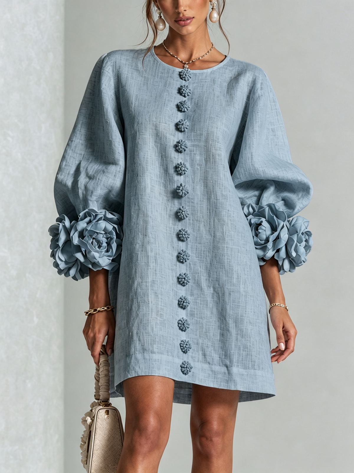 Front view of the light blue dress on a model, showing the round neck, row of textured flower buttons and rosette sleeve trim. 41