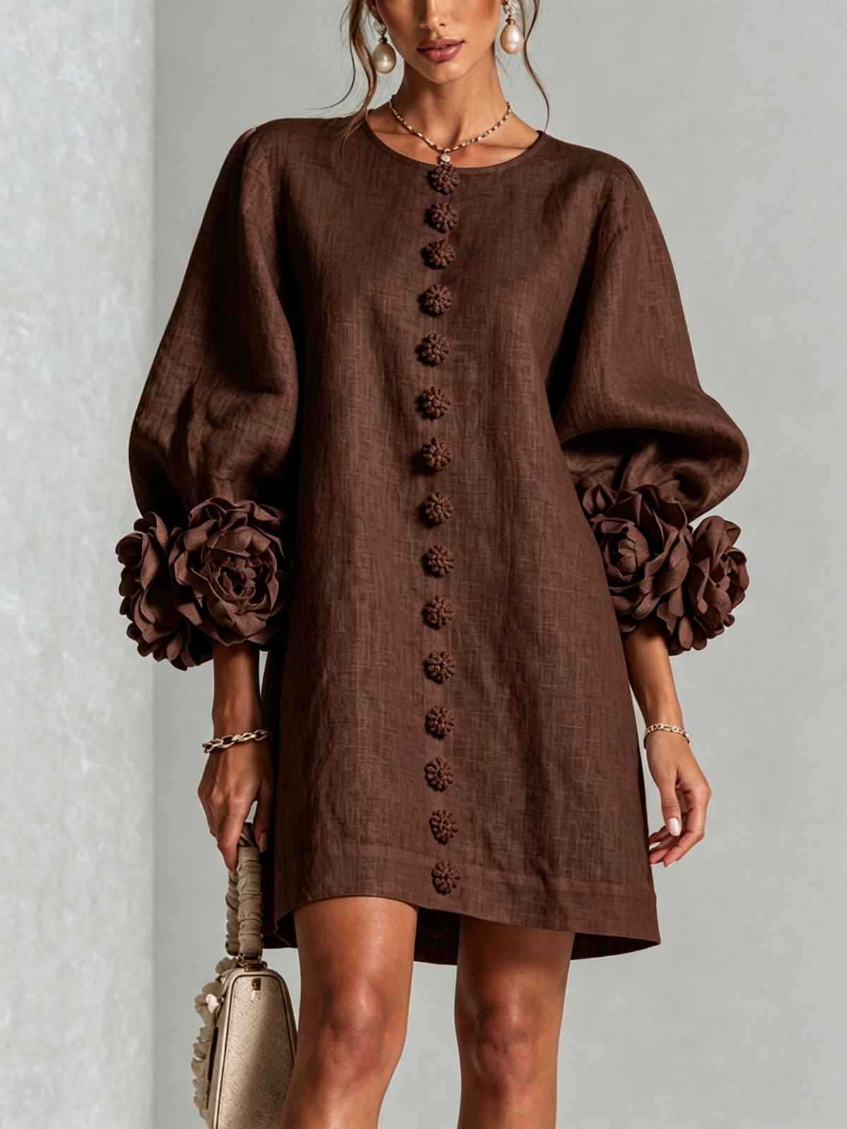 Chocolate brown dress worn by a model, front view, with flower-shaped buttons down the centre and rosettes on the puffed sleeve cuffs. 31