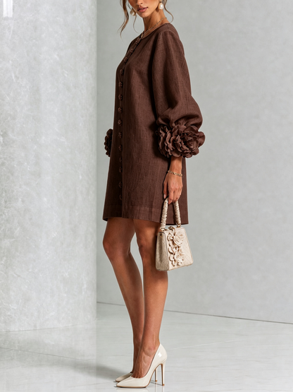 Brown dress in side view on a model holding a small cream handbag, showing the balloon sleeve and rosette cuff. 32