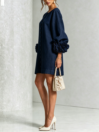 Side view of the navy dress in a studio, showing the button line, balloon sleeve and large rosette cuff, with cream heels. 19