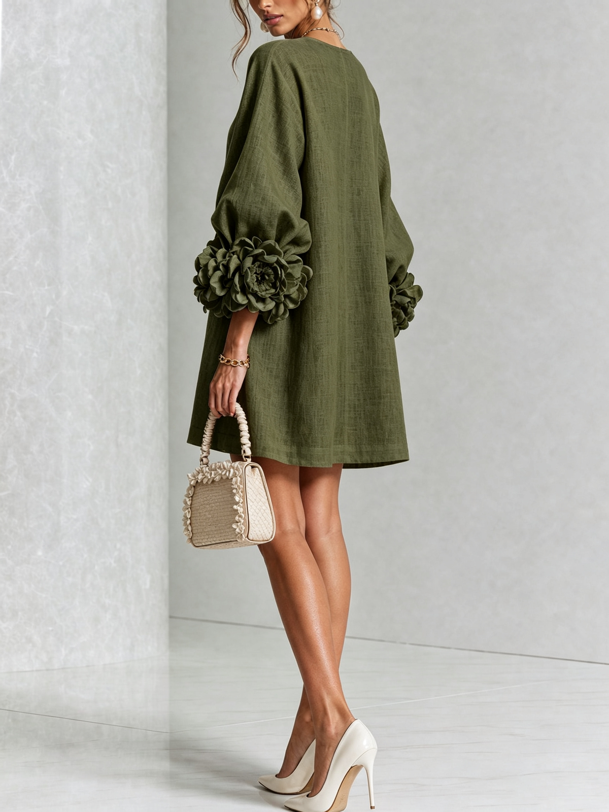 Back view of the olive green dress in a studio, showing the plain back and large rosette cuffs, model holding a woven handbag. 18