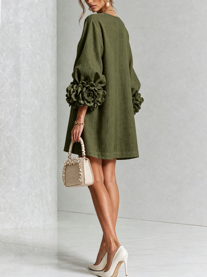 Back view of the olive green dress in a studio, showing the plain back and large rosette cuffs, model holding a woven handbag. 18