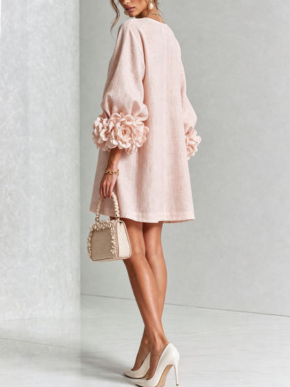Pale pink dress from the back on a model, with a plain loose back and oversized rosette trim on the sleeves. 26