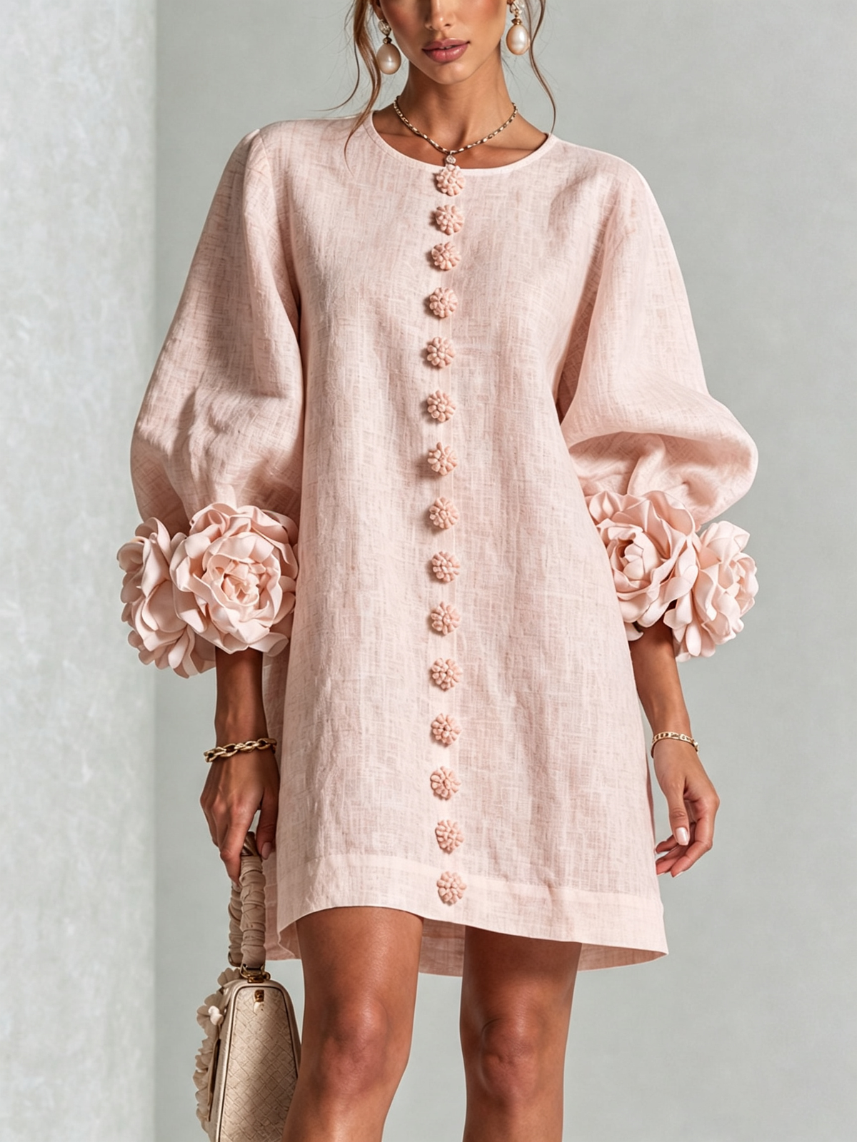 Pale pink dress worn by a model, front view, with a line of flower buttons down the centre and big rosettes at the cuffs. 24