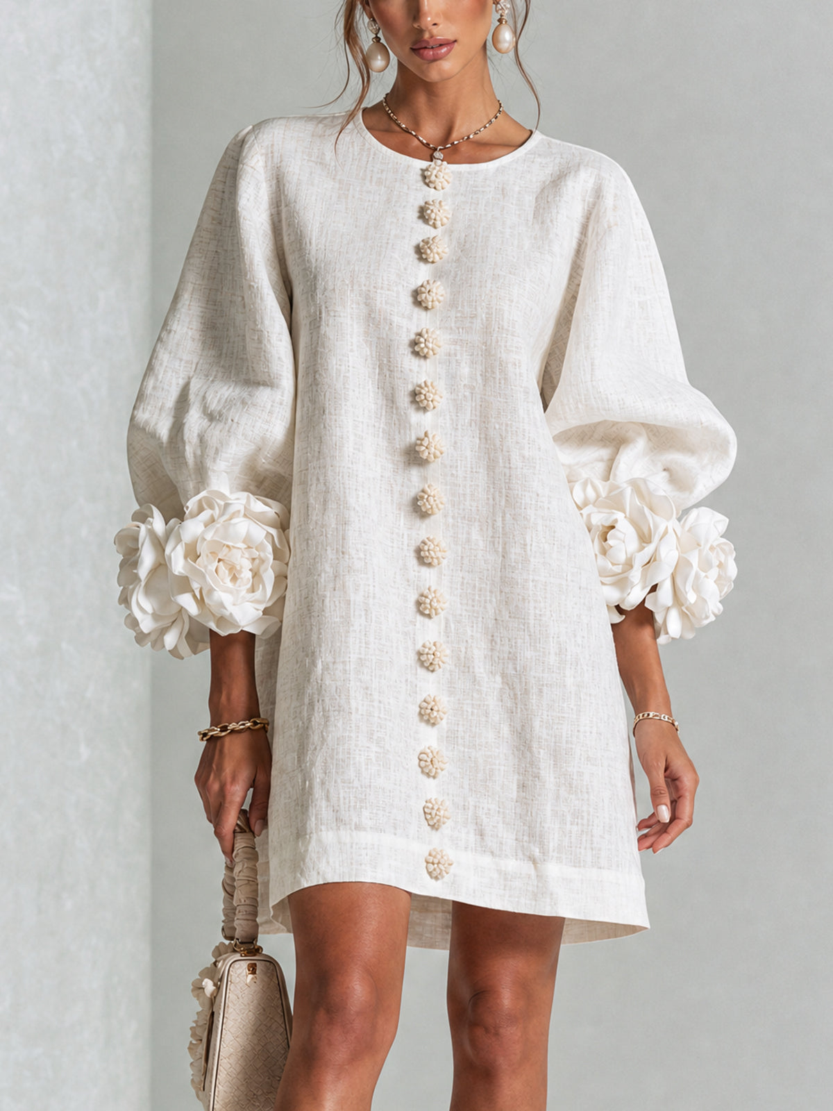 Cream dress on a model in a studio, holding a small handbag, showing the front buttons and large rose cuffs. 10