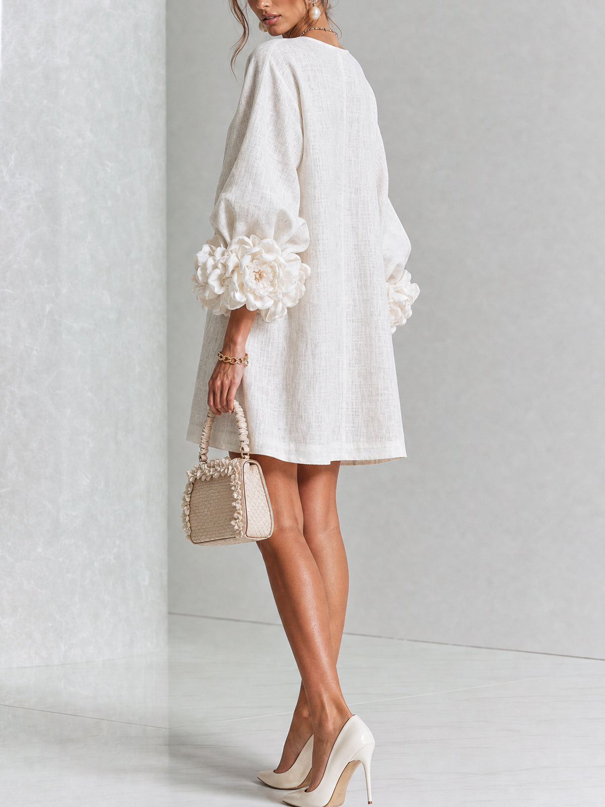 Back and side view of the cream dress in a studio, showing the plain back and rosette cuffs, with a small woven handbag. 14