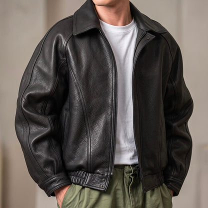 Front view of a man wearing the black grained jacket unzipped over a white T-shirt and green trousers, hands in pockets. 1