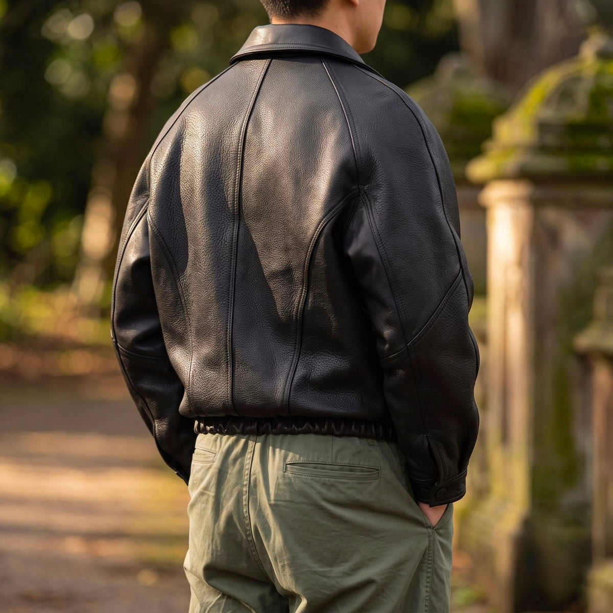Back view of the black jacket worn outdoors with green trousers, showing the panelled back seams and elasticated waistband. 3