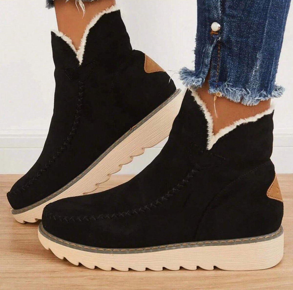 Side view of black suede-look ankle boots with cream fleece trim and a chunky ridged sole, worn with frayed jeans. 1