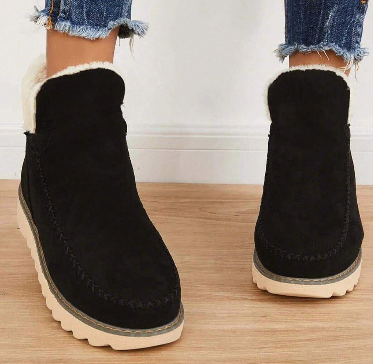 Front view of black slip-on ankle boots with thick white fleece lining at the opening and decorative stitching on the toe. 4