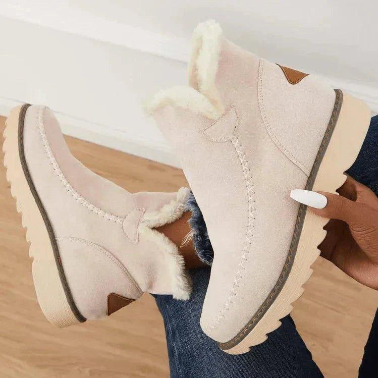 Pair of beige fleece-lined ankle boots held in hand, showing the cross-stitching, small tan heel patch and ridged platform sole. 6
