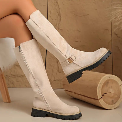 Cream suede-look knee-high boots worn by a model, showing the side zip, gold buckle strap and chunky black sole. 8