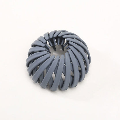 Single matte slate blue spiral bird's-nest clip on a plain pale background, with its inner prongs visible in the centre. 6
